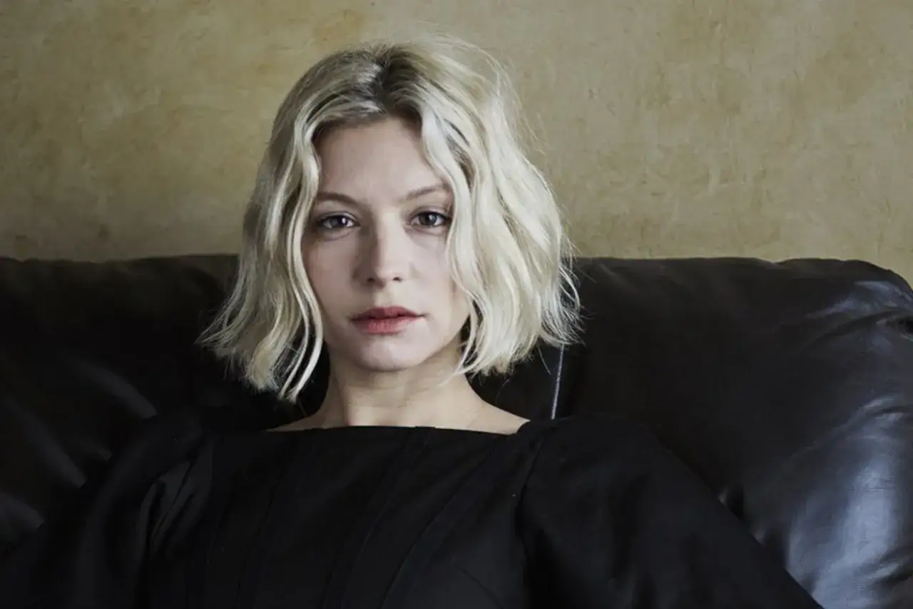 Kobieta z blond włosami w stylu blunt bob, w czarnej sukience, siedzi na skórzanej kanapie.