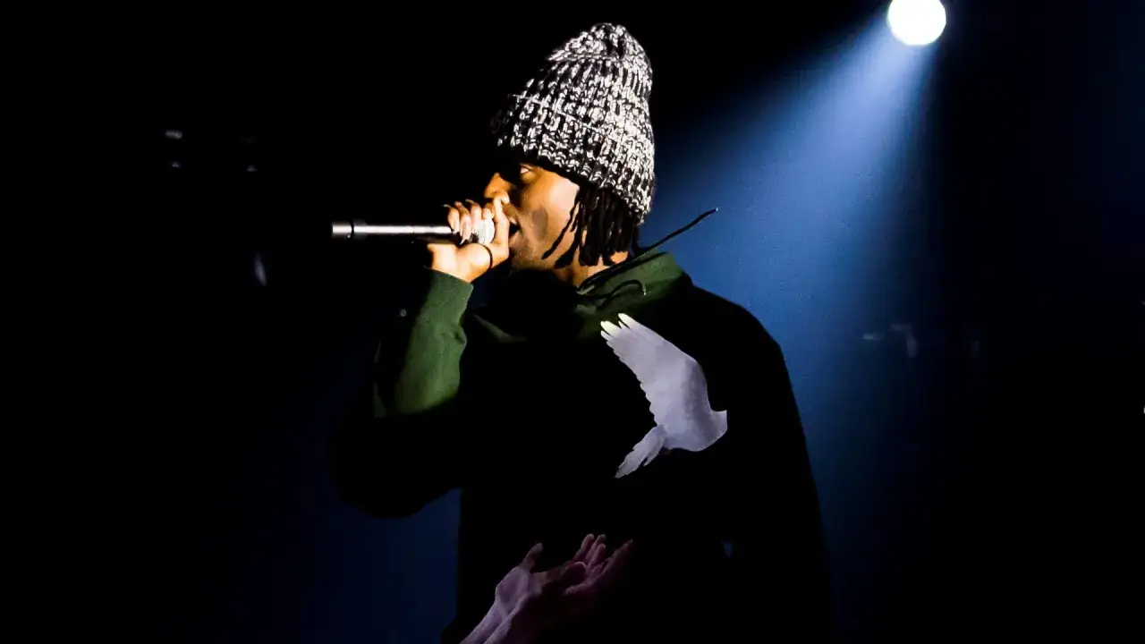 Playboi Carti Polska na scenie, w czapce i zielonej bluzie z gołębiem.