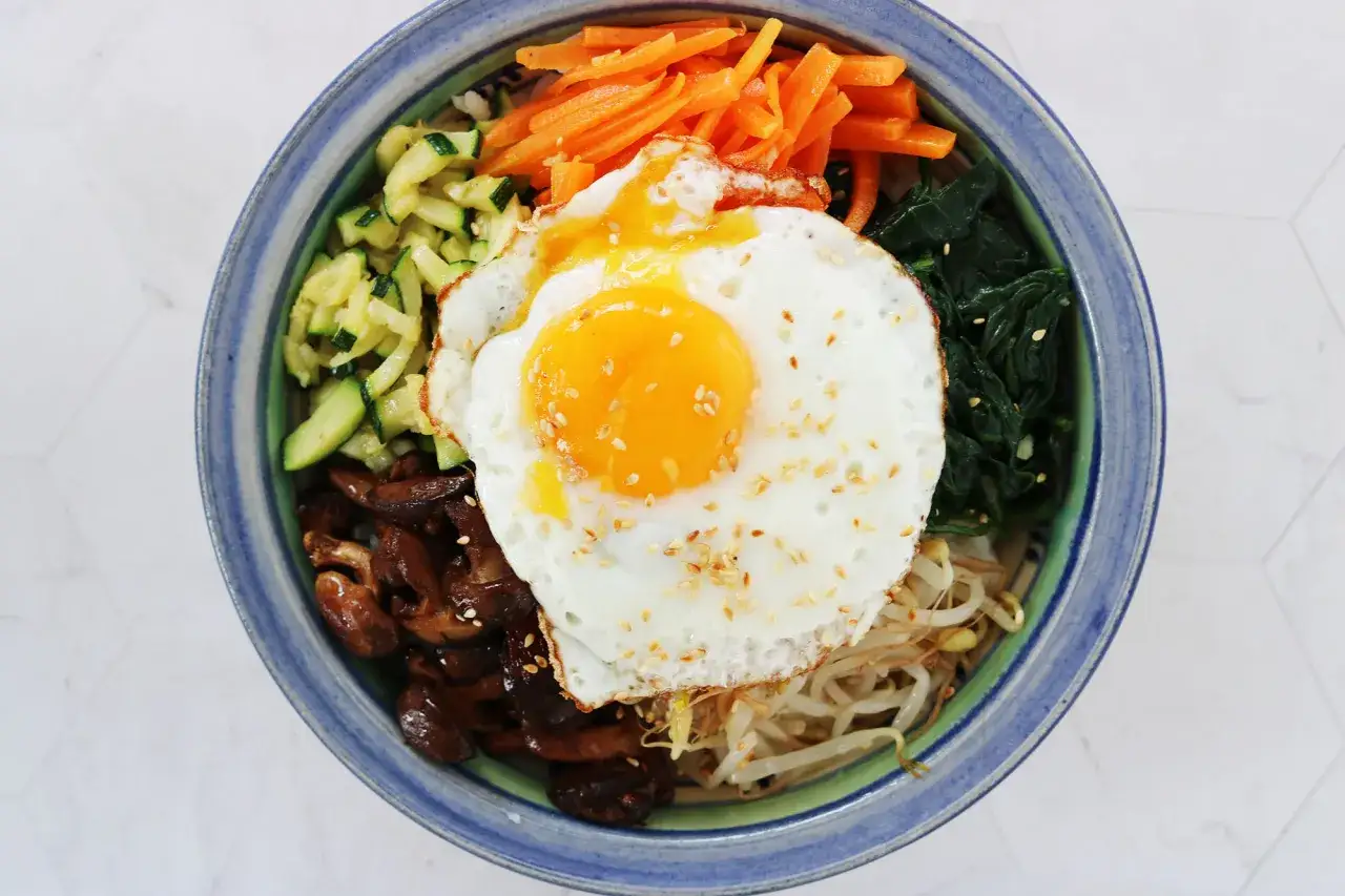 En skål med bibimbap recept: ris, grönsaker, svamp och ett stekt ägg med rinnig gula.