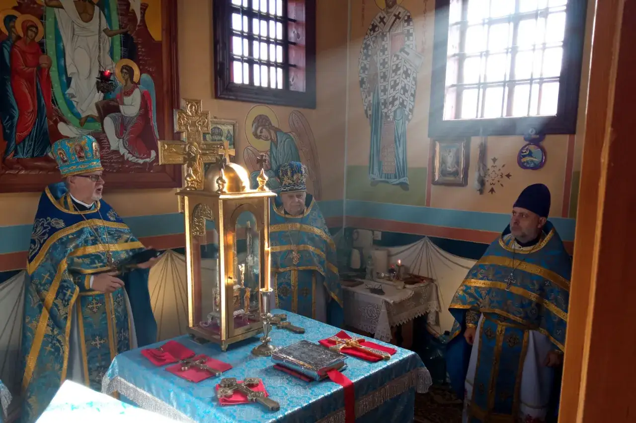 Trzech duchownych w szatach liturgicznych podczas nabożeństwa. W centrum ołtarz z relikwiarzem i księgą. Widoczne ikony i okna. Ortodoksja w pełnej krasie.