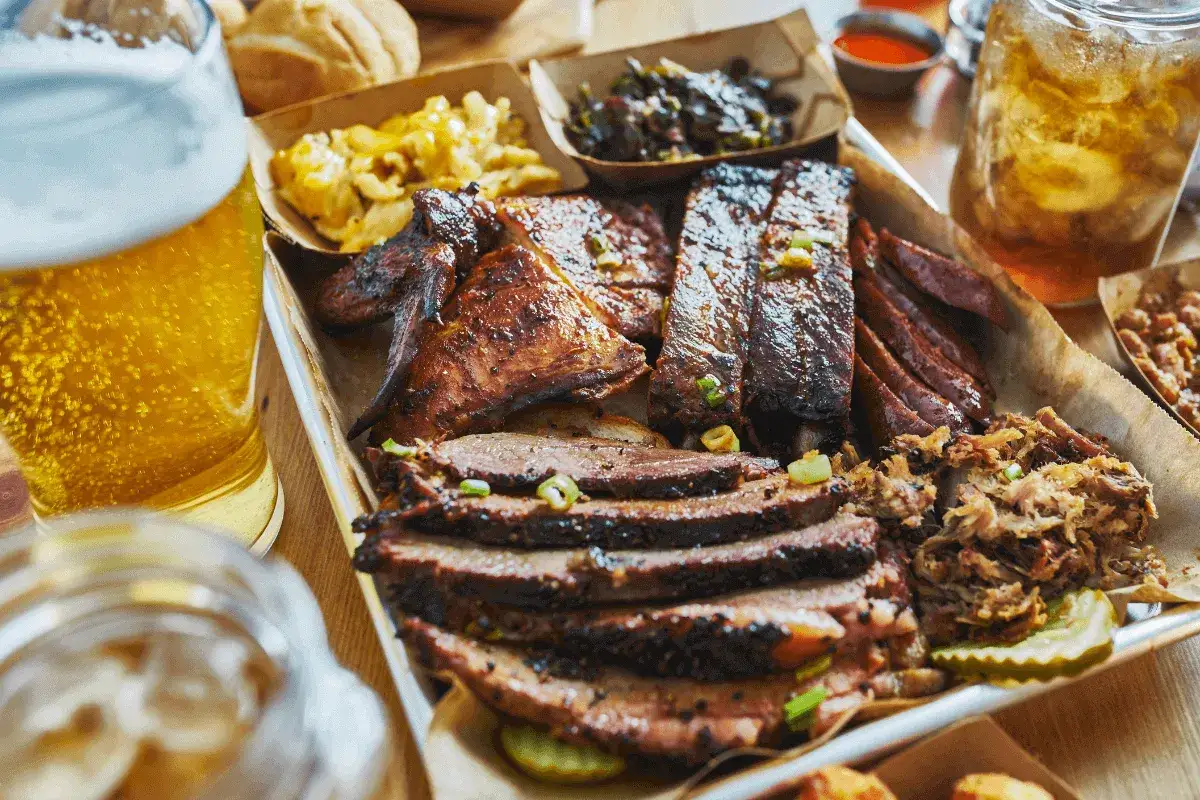Szaszłyki z karkówki, żeberka, brisket i pulled pork na tacy z dodatkami. Obok piwo i napój.