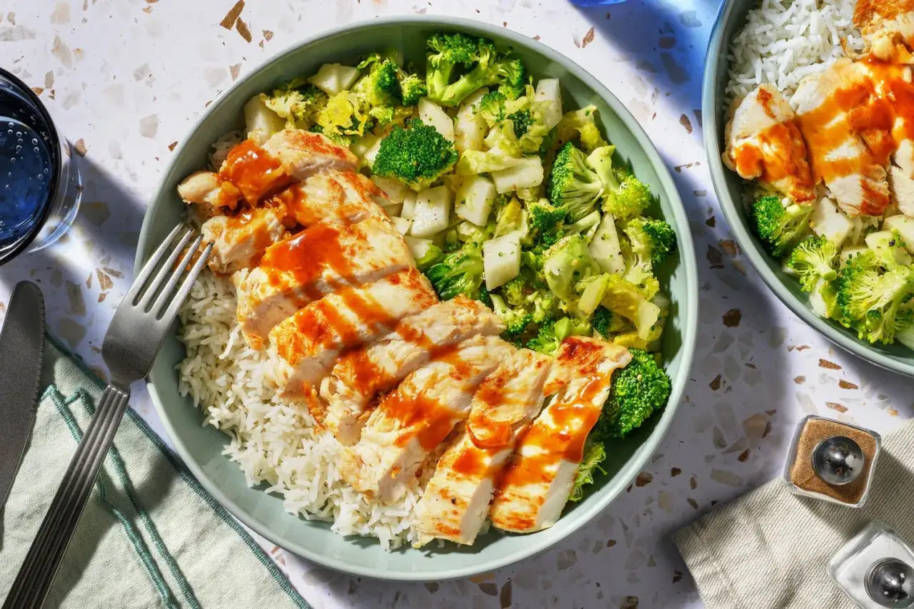 Skivad kyckling med en klibbig, glansig s&aring;s serveras med ris och broccoli.
