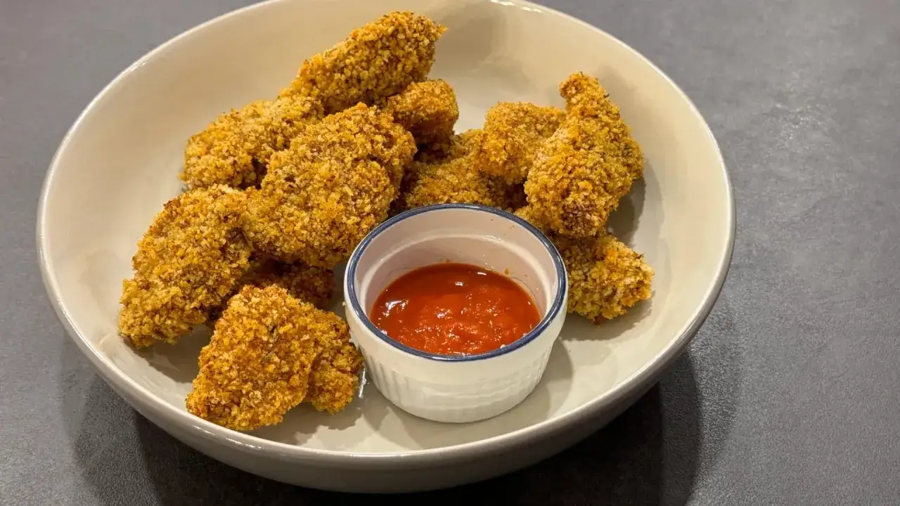 Krispiga chicken nuggets i en skål med en liten skål med röd dippsås. Perfekt för en snabb och god måltid.