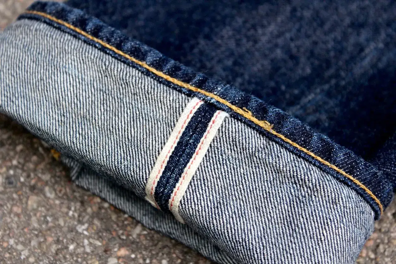 Close-up of a rolled-up denim cuff, showcasing the selvedge edge with its iconic red and white stripe, a hallmark of quality jean stitch.