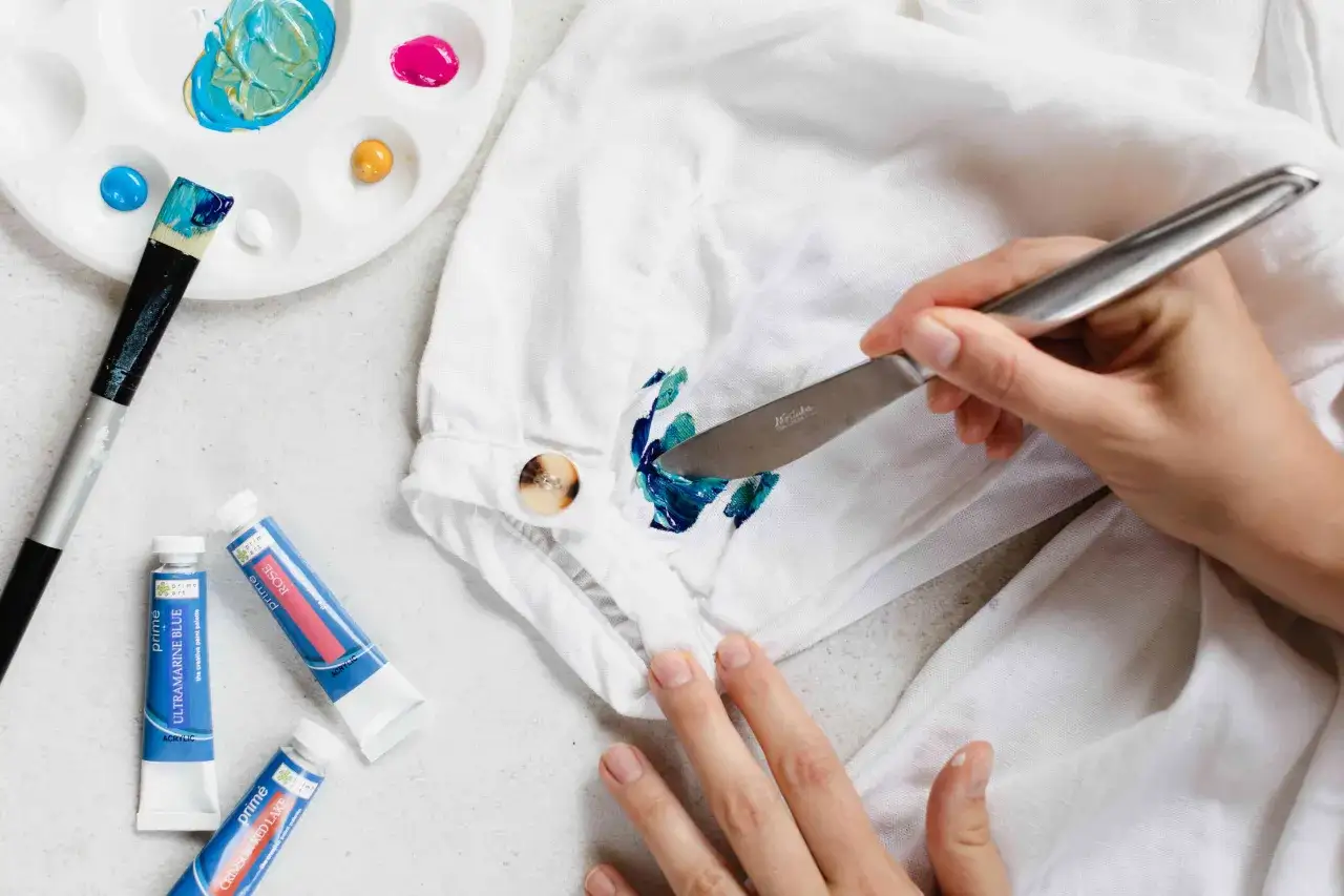 Application d'acrylique sur un tissu blanc avec une spatule. Palette avec des couleurs vives et des tubes de peinture acrylique à proximité.