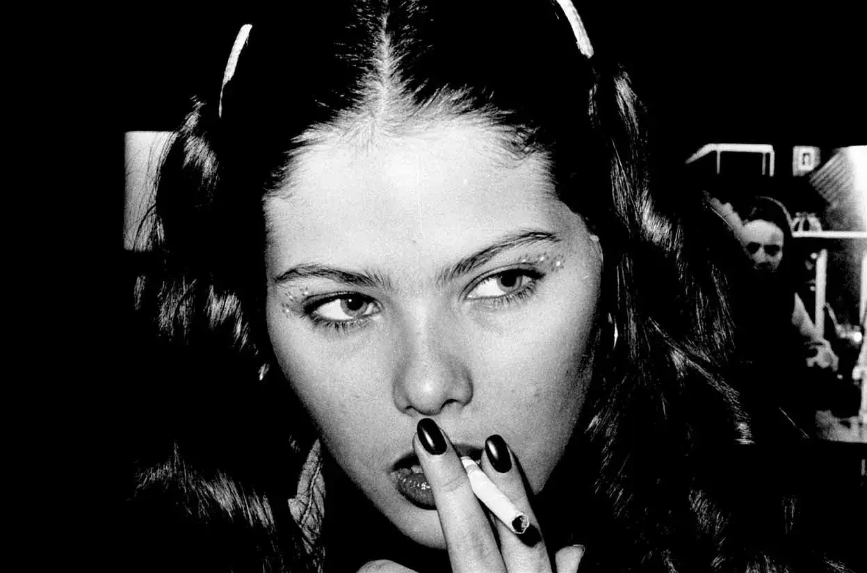 Ritratto di una giovane donna con trucco scintillante e sigaretta, evocativa delle attrici italiane di teatro degli anni '70.