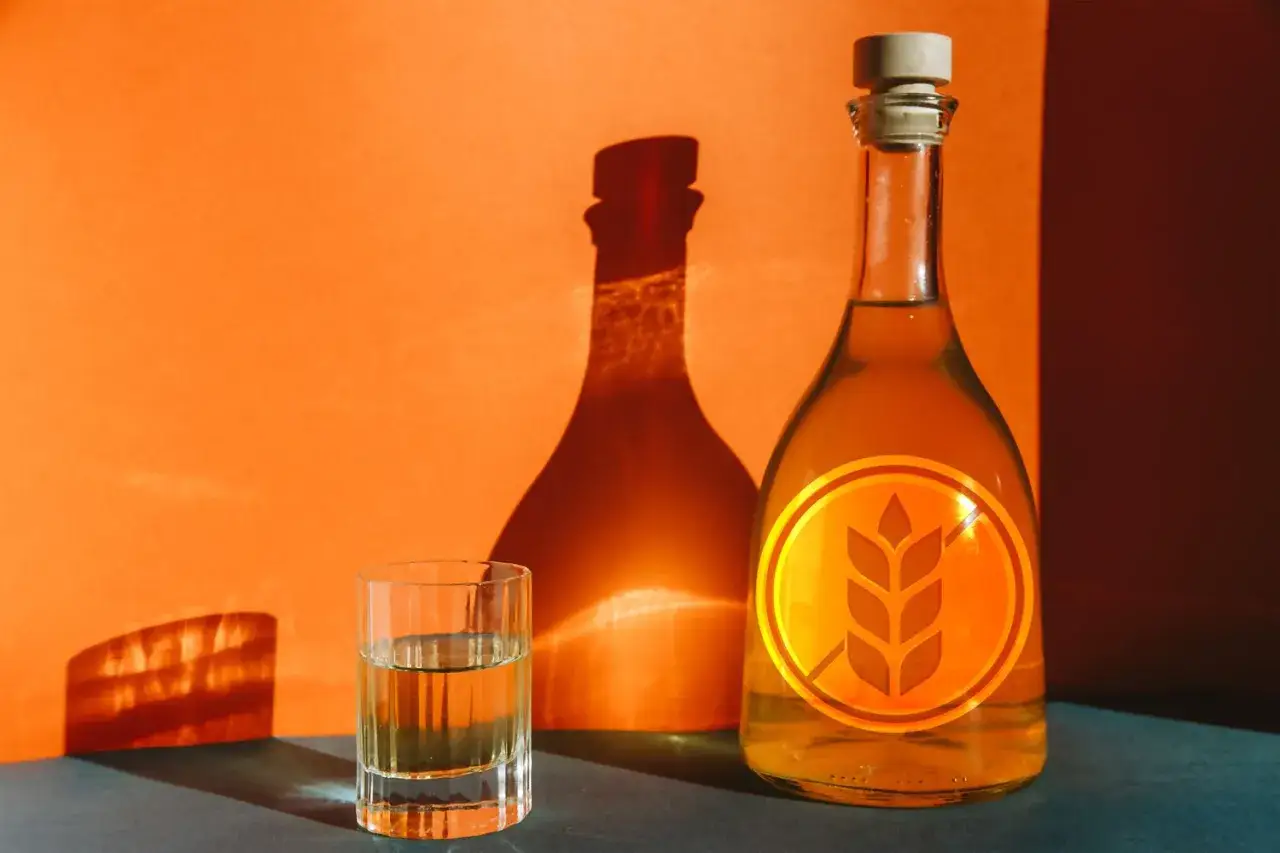 Flasche und Glas mit bernsteinfarbenem Getr&auml;nk, das Symbol f&uuml;r **whiskey glutenfrei** auf der Flasche.