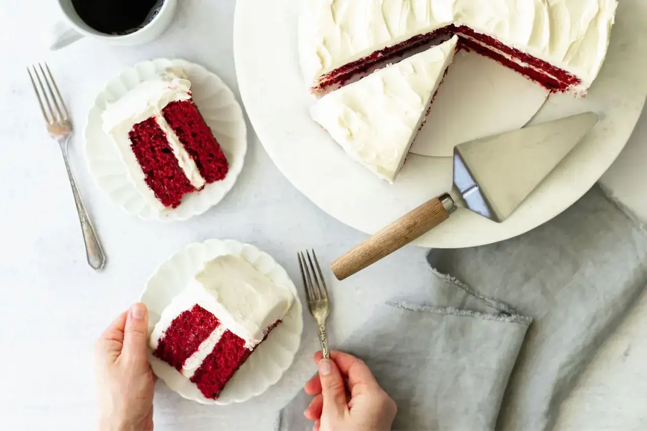 En saftig red velvet cake med krämig frosting. Två bitar är upplagda på vita fat, redo att avnjutas.