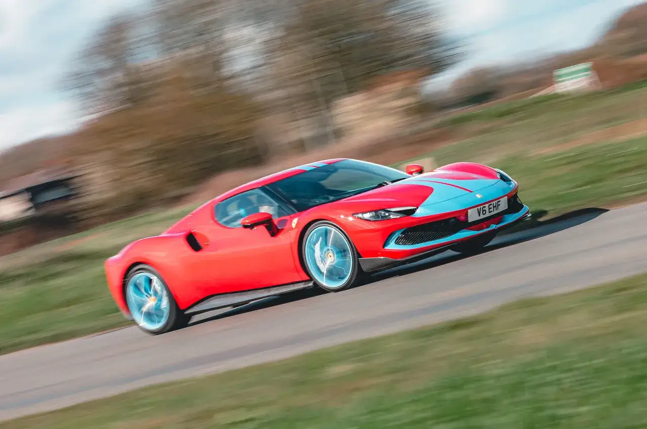 Czerwone Ferrari 296 GTB z niebieskimi pasami pędzi po krętej drodze, rozmazując tło.