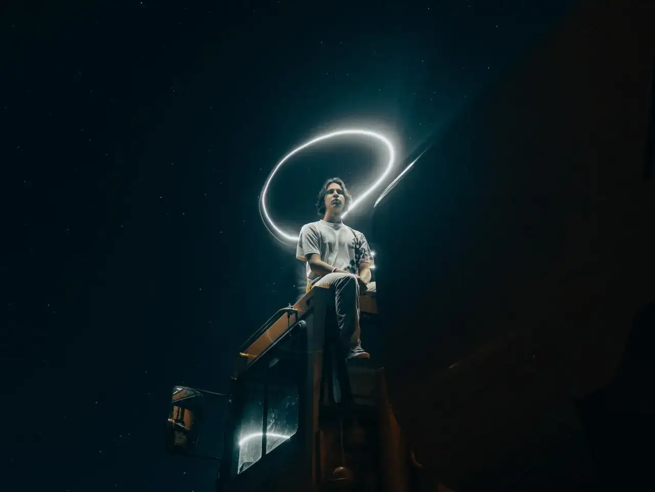 Młody mężczyzna siedzi na maszynie budowlanej nocą, otoczony świetlnym kręgiem. Inspiracja do tworzenia ciekawe filmy.