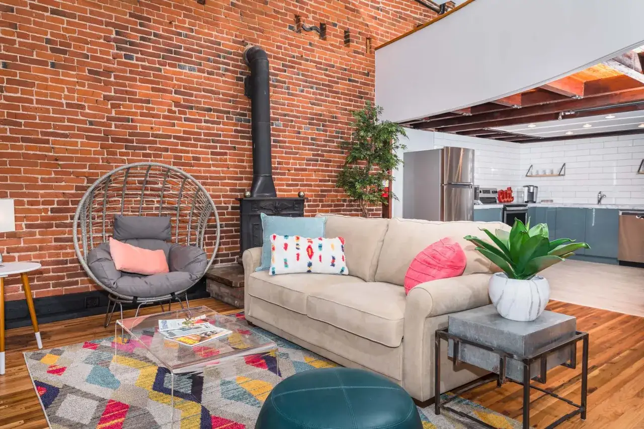 Nowoczesny salon z ceglaną ścianą, kominkiem i kuchnią w tle. Idealne miejsce na pobyt, zastanawiasz się airbnb co to? To platforma do wynajmu krótkoterminowego.