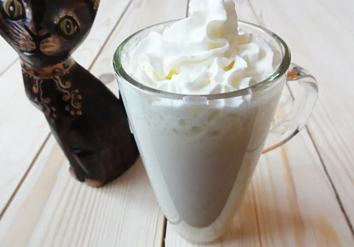 Pyszny koktajl bananowy z bitą śmietaną, obok siedzi czarny kotek.