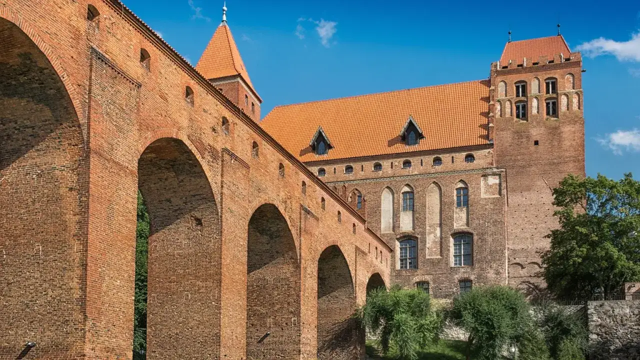 Potężny zamek w Kwidzynie z ceglanymi arkadami i wieżami pod błękitnym niebem.