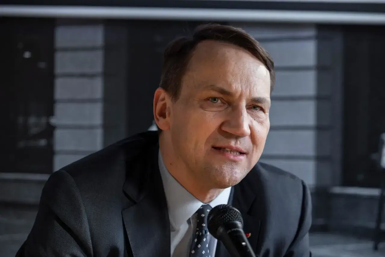 Jan Sikorski, ojciec Radosława Sikorskiego, w garniturze i krawacie, mówi do mikrofonu.