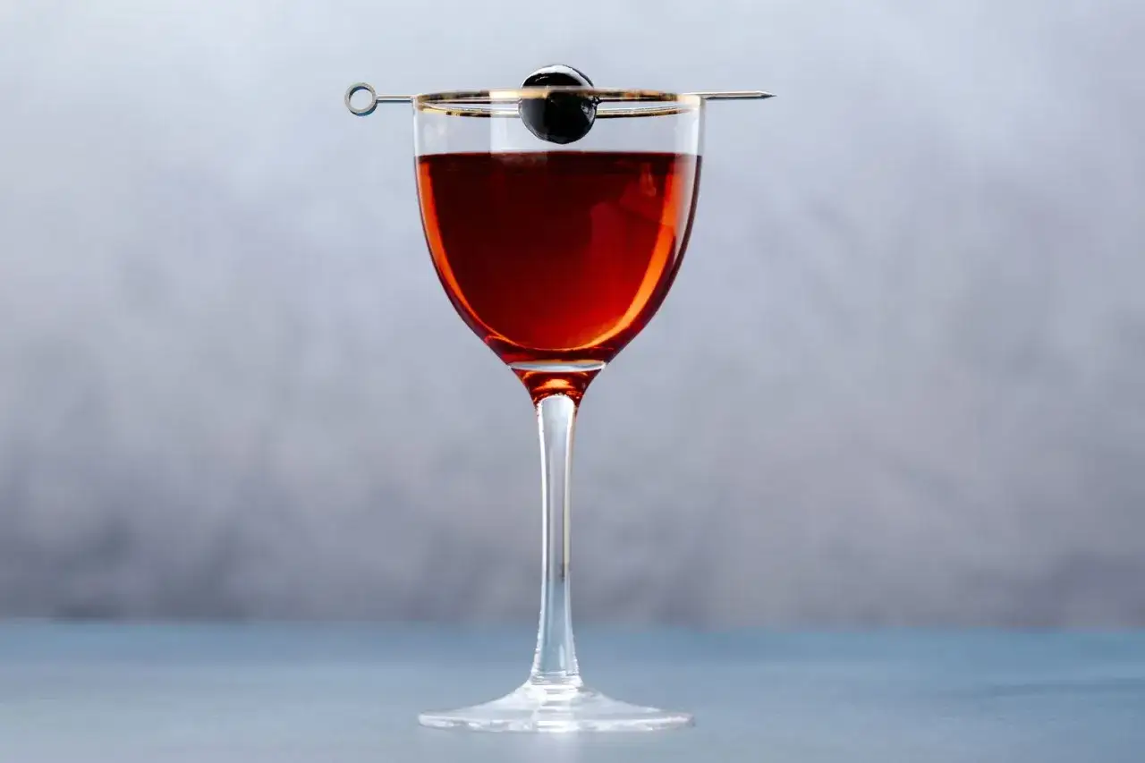 Elegancki drink Rob Roy w kieliszku, ozdobiony wiśnią na wykałaczce.