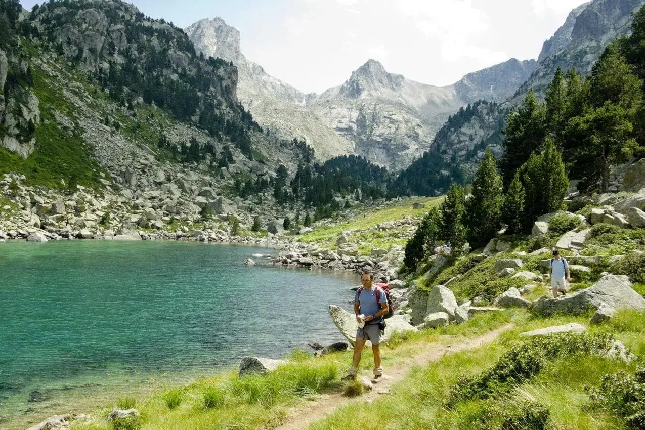 A man with a backpack enjoys walking Spain's stunning mountain scenery by a turquoise lake.