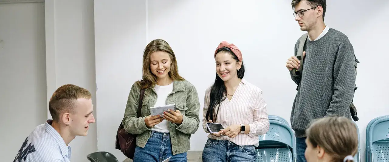 Grupa młodych ludzi dyskutuje, jak przygotować się do pracy w branży marketingowej. Uśmiechnięci, z notatnikami i telefonami, planują swoją przyszłość.