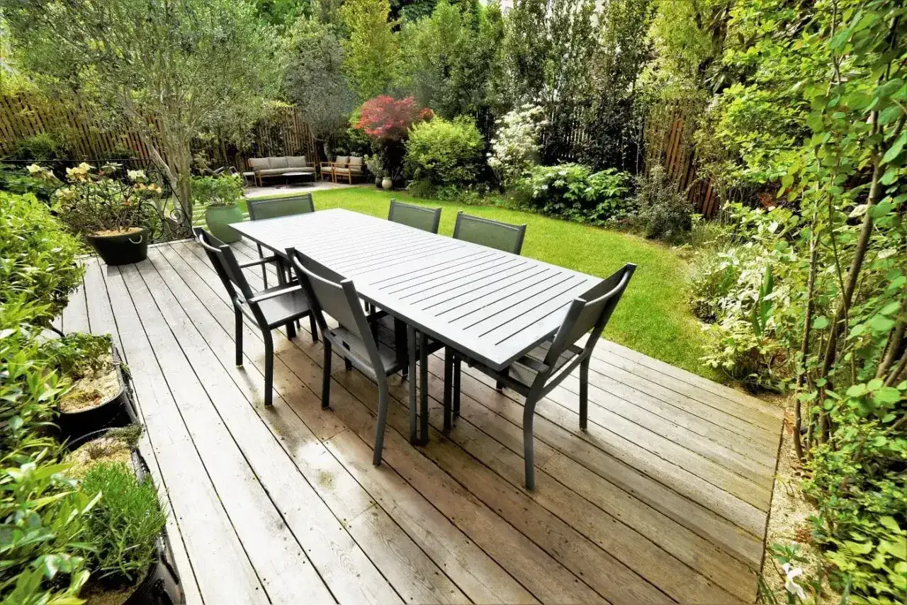 Table et chaises sur une terrasse en bois, entour&eacute;es d'un jardin verdoyant. Un bel am&eacute;nagement ext&eacute;rieur pour profiter des beaux jours.