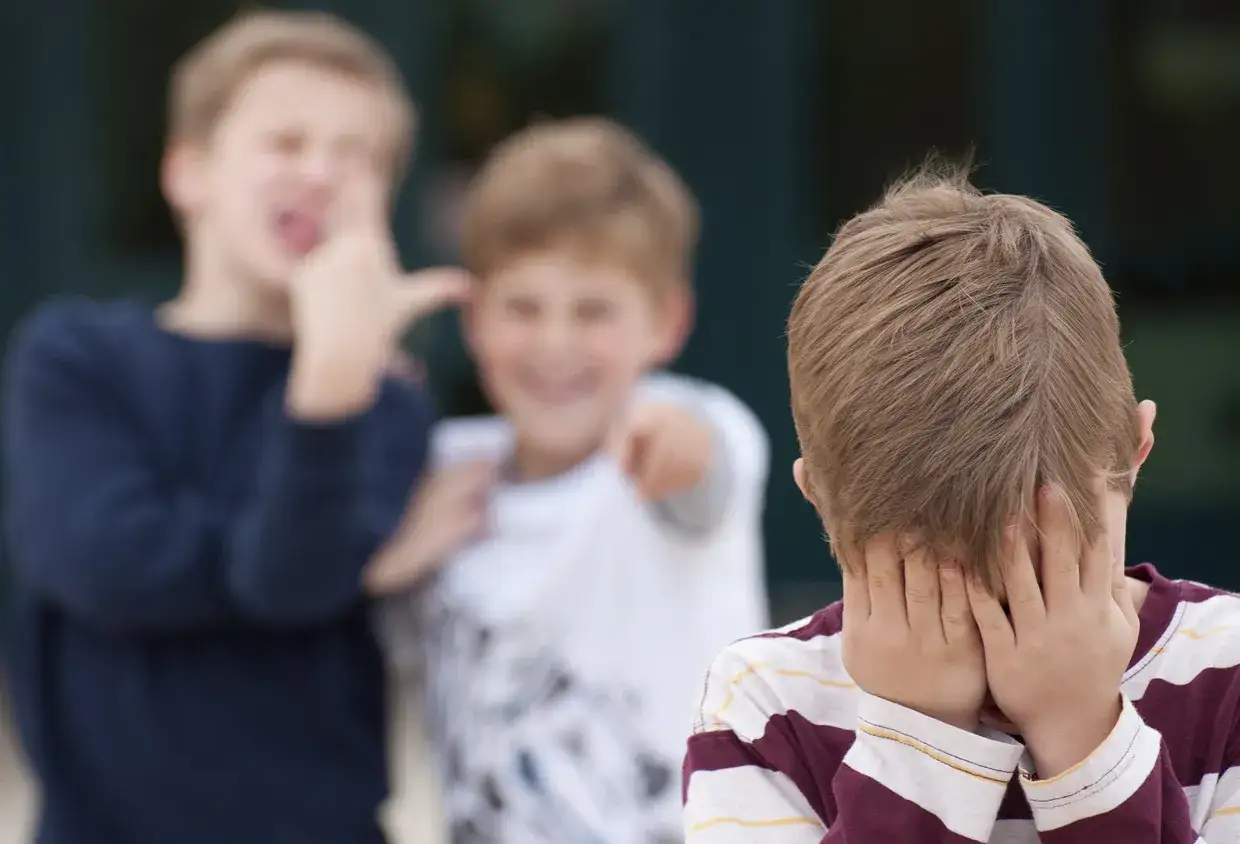 Ein Junge versteckt sein Gesicht, während zwei andere ihn verspotten. Ein trauriges Bild von **Konflikten in der Schule**.