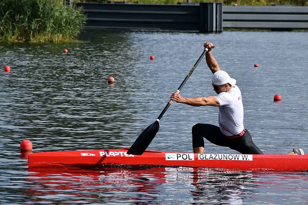Mistrz Polski w kajakarstwie, W. Głązunow, w czerwnej łodzi, wiosłuje na wodzie.