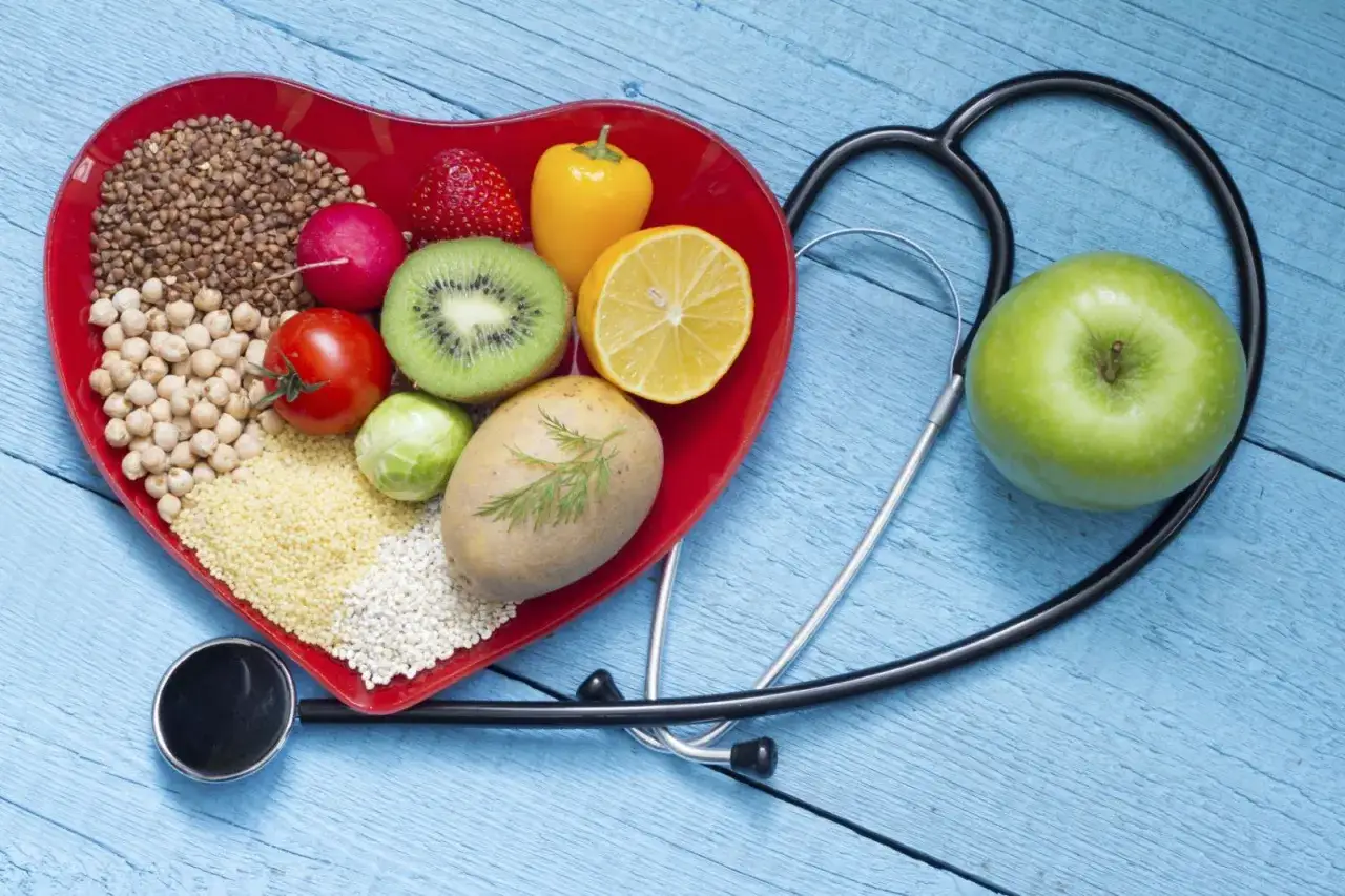 Zdrowa dieta, pełna owoc&oacute;w, warzyw i ziaren, to klucz do tego, jak obniżyć cholesterol. Stetoskop symbolizuje troskę o serce.