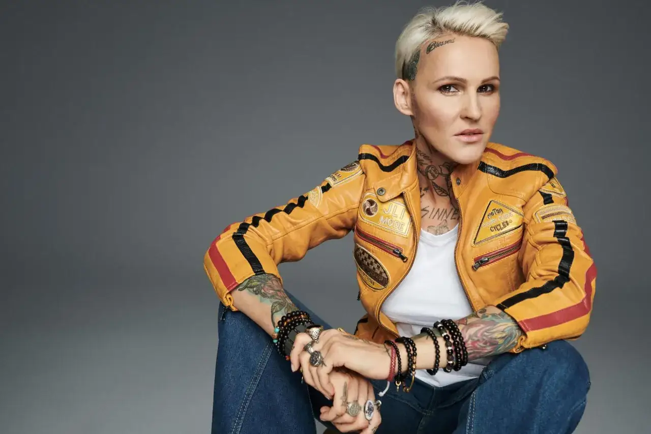 Agnieszka Chylińska w żółtej kurtce motocyklowej, z tatuażami i biżuterią. 