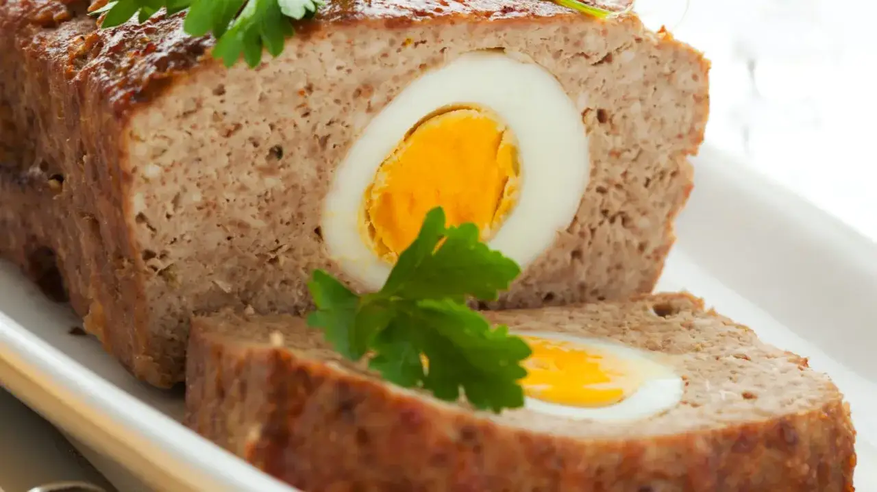 Kawałek klasycznej pieczeni rzymskiej z widocznym w środku jajkiem na twardo, ozdobiony natką pietruszki.