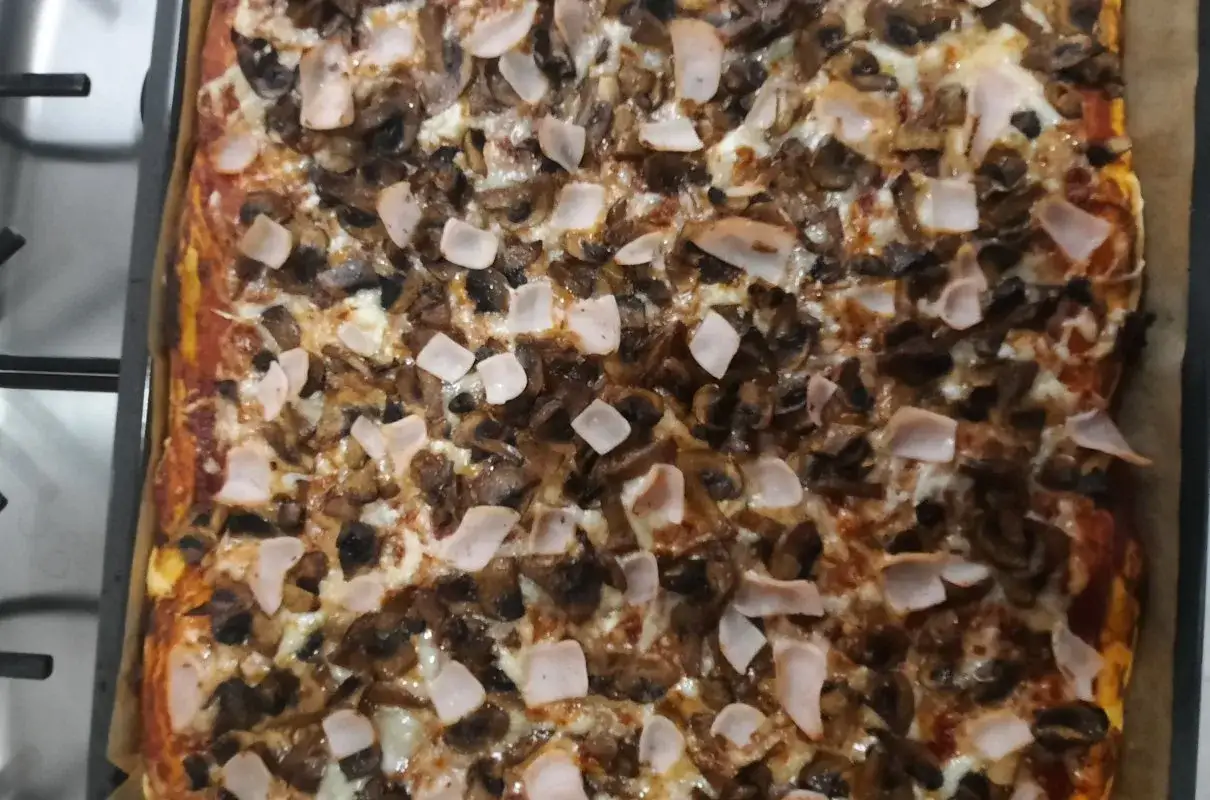 Pyszna pizza z pieczarkami i szynką, prosto z pieca nagrzanego do 180 stopni. Idealna na szybki obiad.