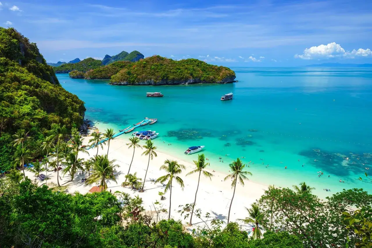 Rajska plaża w Ang Thong National Marine Park, z turkusową wodą, palmami i łodziami.