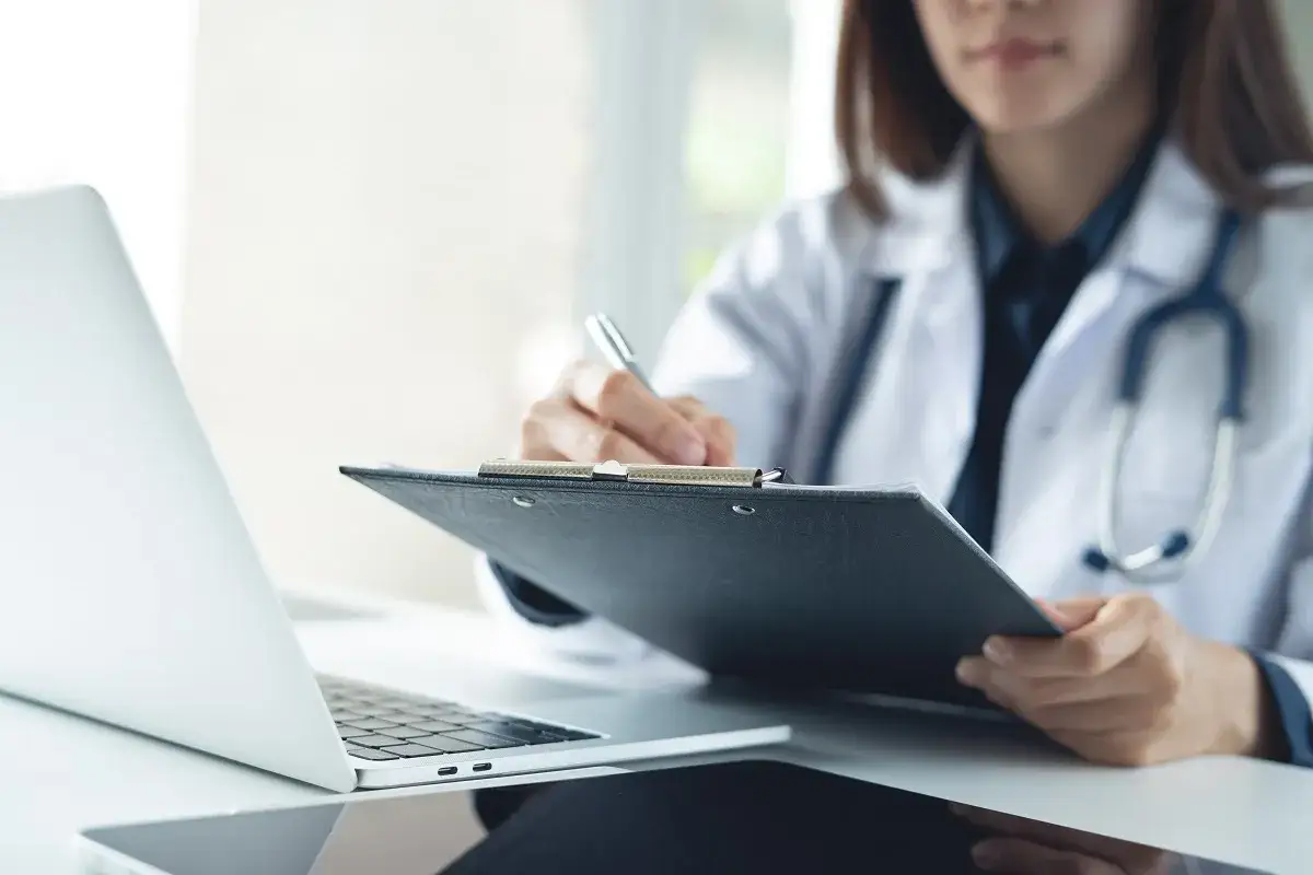 Medico con stetoscopio scrive su cartella clinica, accanto a un laptop. Un caso di omicidio colposo medico potrebbe emergere da una negligenza.