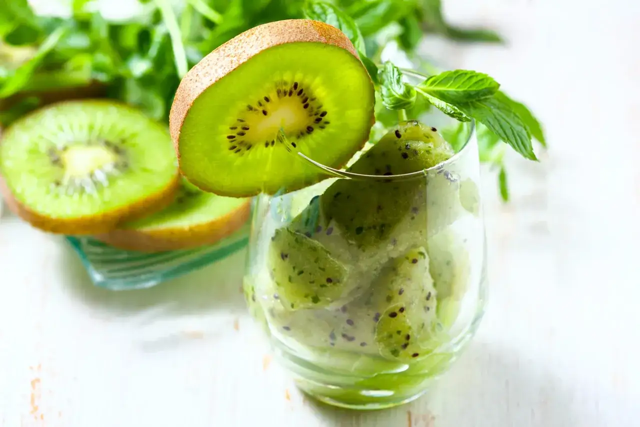 Mrożone kiwi w szklance z miętą i plasterkami kiwi obok. Świetny sposób, co zrobić z dużą ilością kiwi!