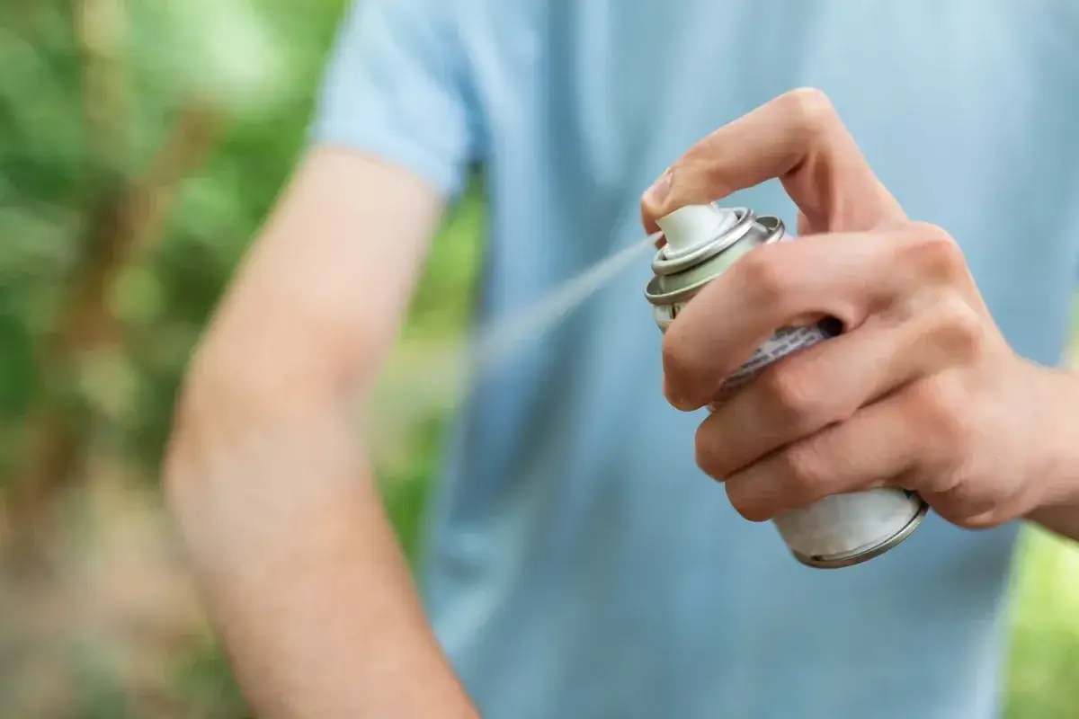 Ręka aplikuje spray na skórę, pokazując, co odstrasza kleszcze.