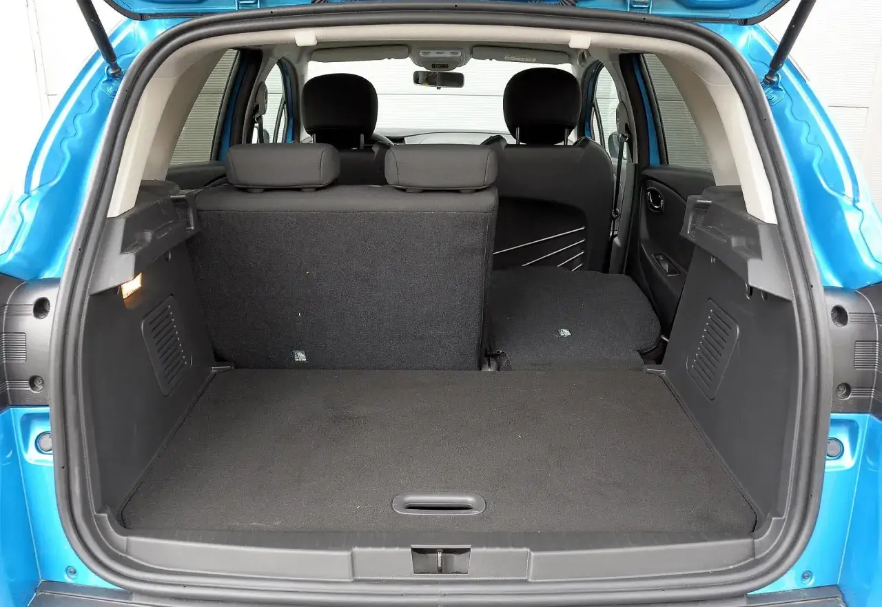 Błękitny Renault Captur 2015 z otwartym bagażnikiem. Widoczne rozłożone tylne siedzenia, tworzące płaską przestrzeń bagażową.
