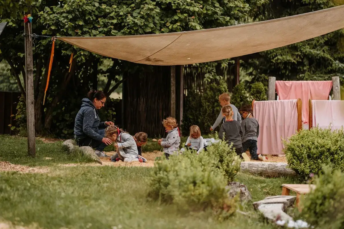Kinder spielen im Sandkasten, eine Erzieherin hilft. Vielleicht sind die Nachteile eines Waldorfkindergartens, dass Kinder wenig Spielzeug haben?