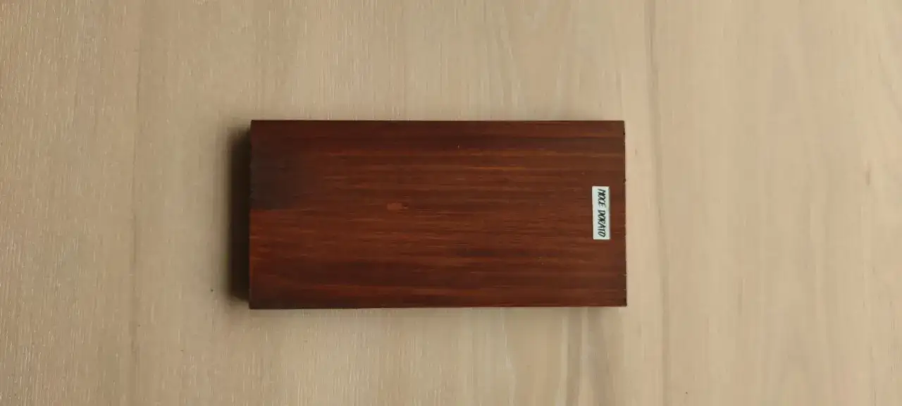 Tavoletta di legno scuro, pronta per essere colorata. La venatura del legno è visibile, con un'etichetta bianca che riporta la scritta