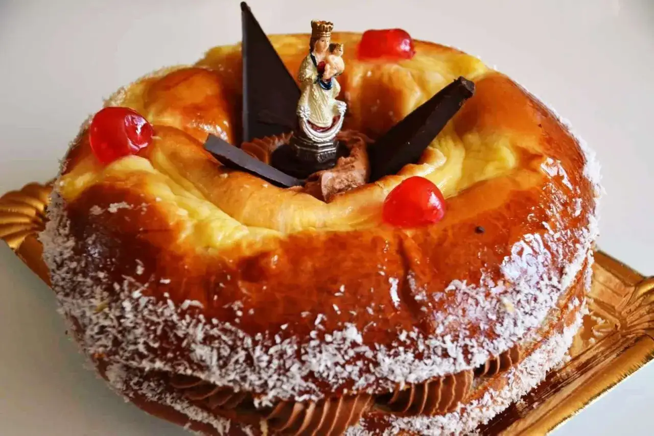 Rosca de la Almudena decorada con una figura de la Virgen, cerezas rojas, chocolate y coco rallado.