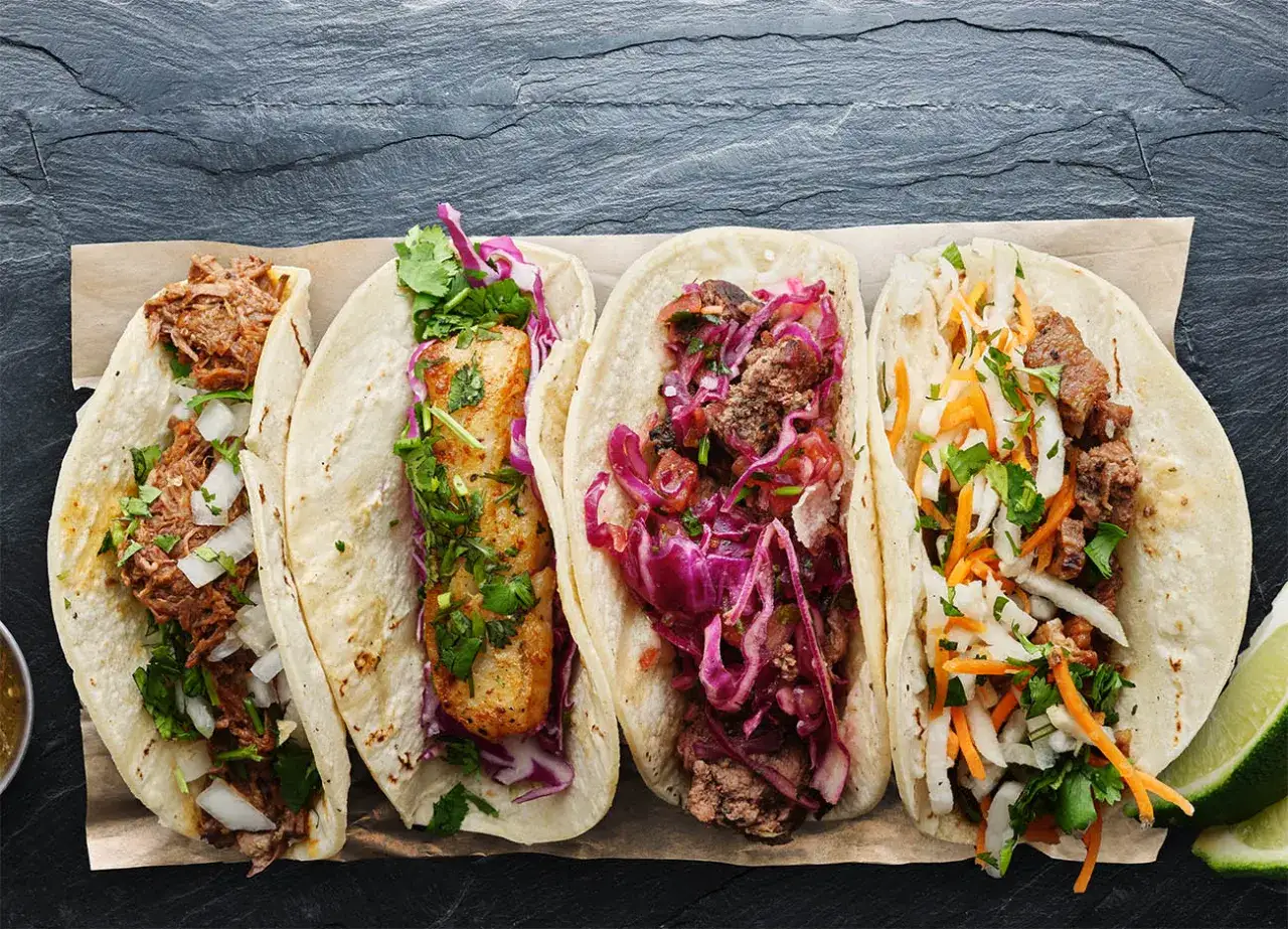 Fyra läckra tacos på en rad: en med kött, en med fisk, en med kött och rödkål, och en med strimlad kål och morot.