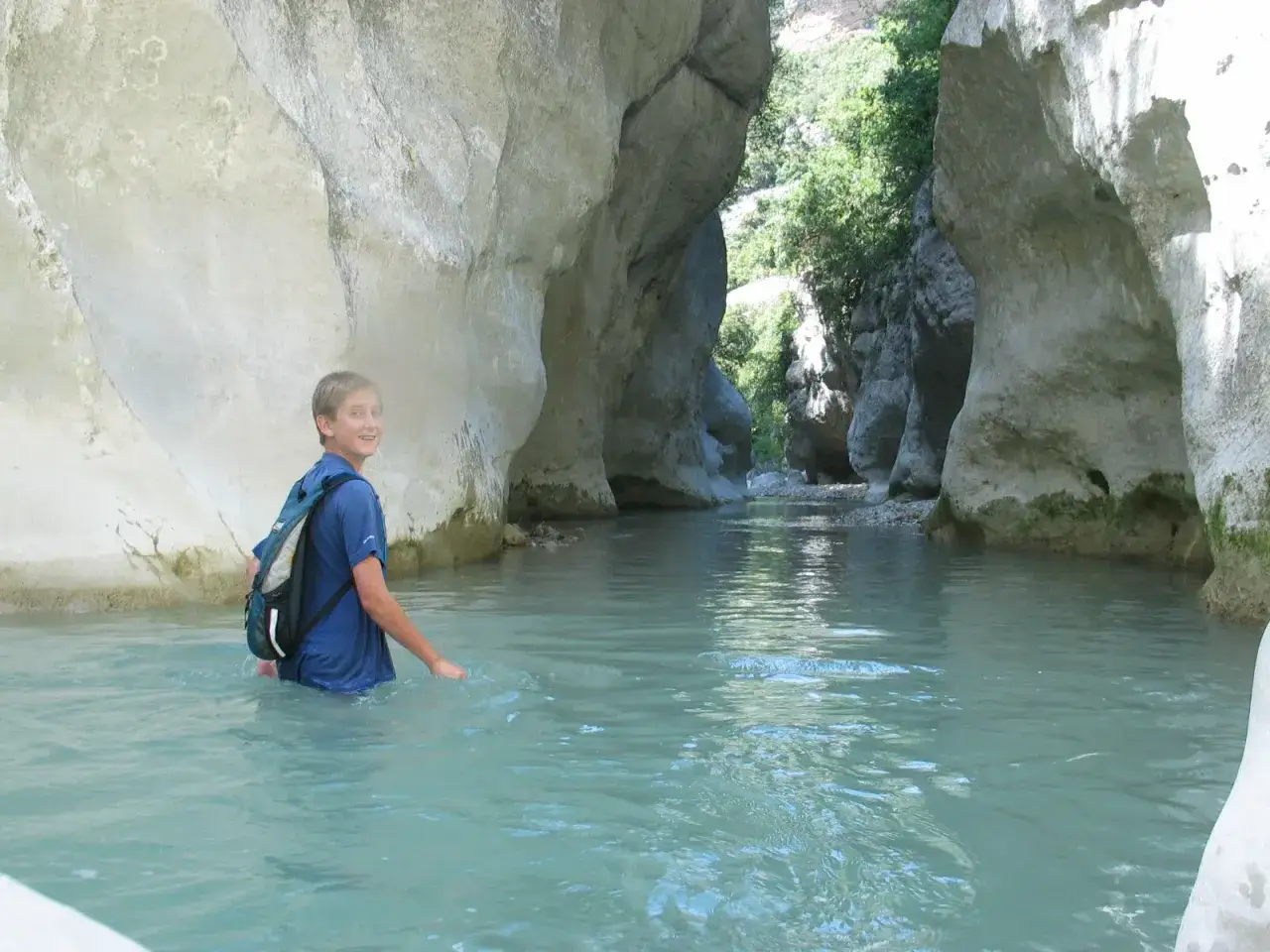 Un jeune garçon avec un sac à dos explore la gorge du Toulourenc, marchant dans l'eau turquoise entre les falaises calcaires.