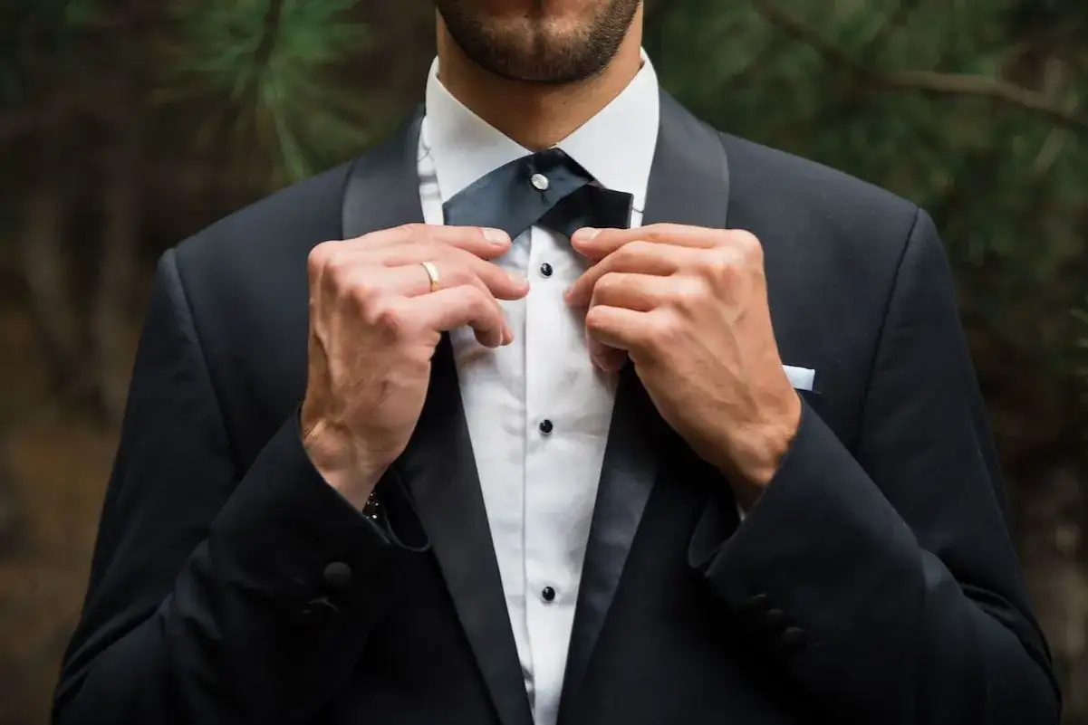 Mann richtet seine Fliege, tr&auml;gt einen eleganten Lounge Suit mit wei&szlig;em Hemd und Manschettenkn&ouml;pfen.