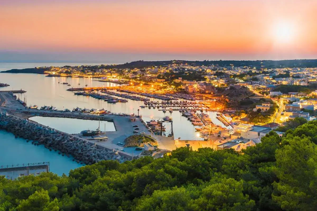 Un incantevole porto turistico illuminato al tramonto, con barche ormeggiate e una citt&agrave; costiera che si estende sulla collina. Un vero gioiello del Salento citt&agrave;.