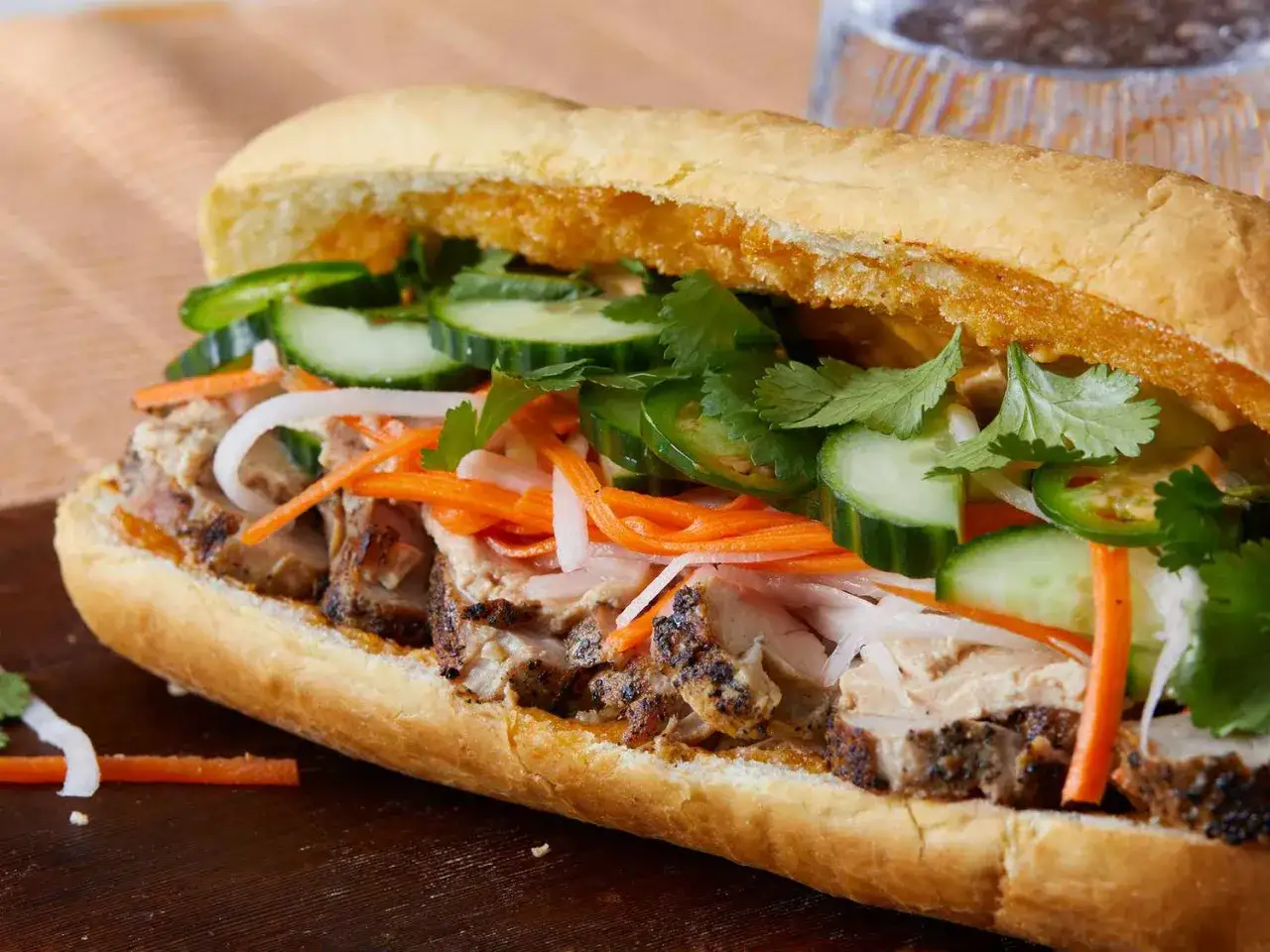 En saftig banh mi med grillat fläsk, krispig gurka, morötter, jalapeños och koriander. Ett perfekt banh mi recept för en smakrik lunch.