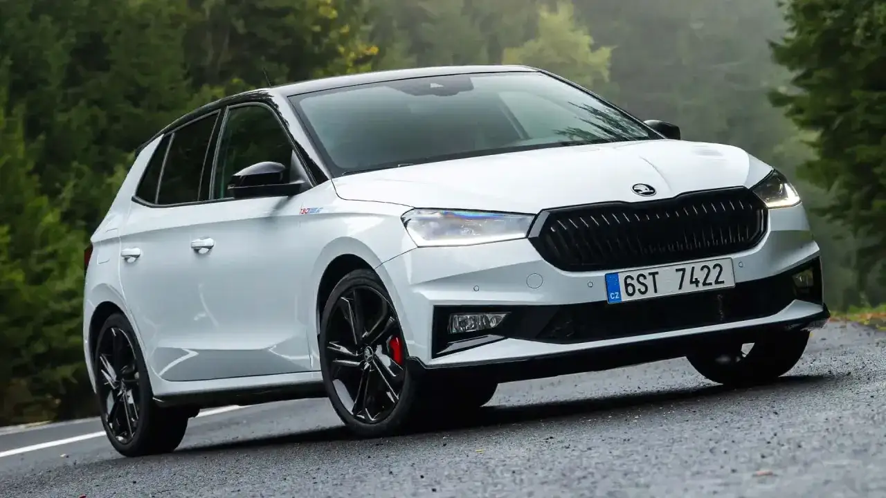 Un Skoda Fabia 130 blanco con techo negro, llantas deportivas y detalles rojos, circulando por una carretera rodeada de &aacute;rboles.