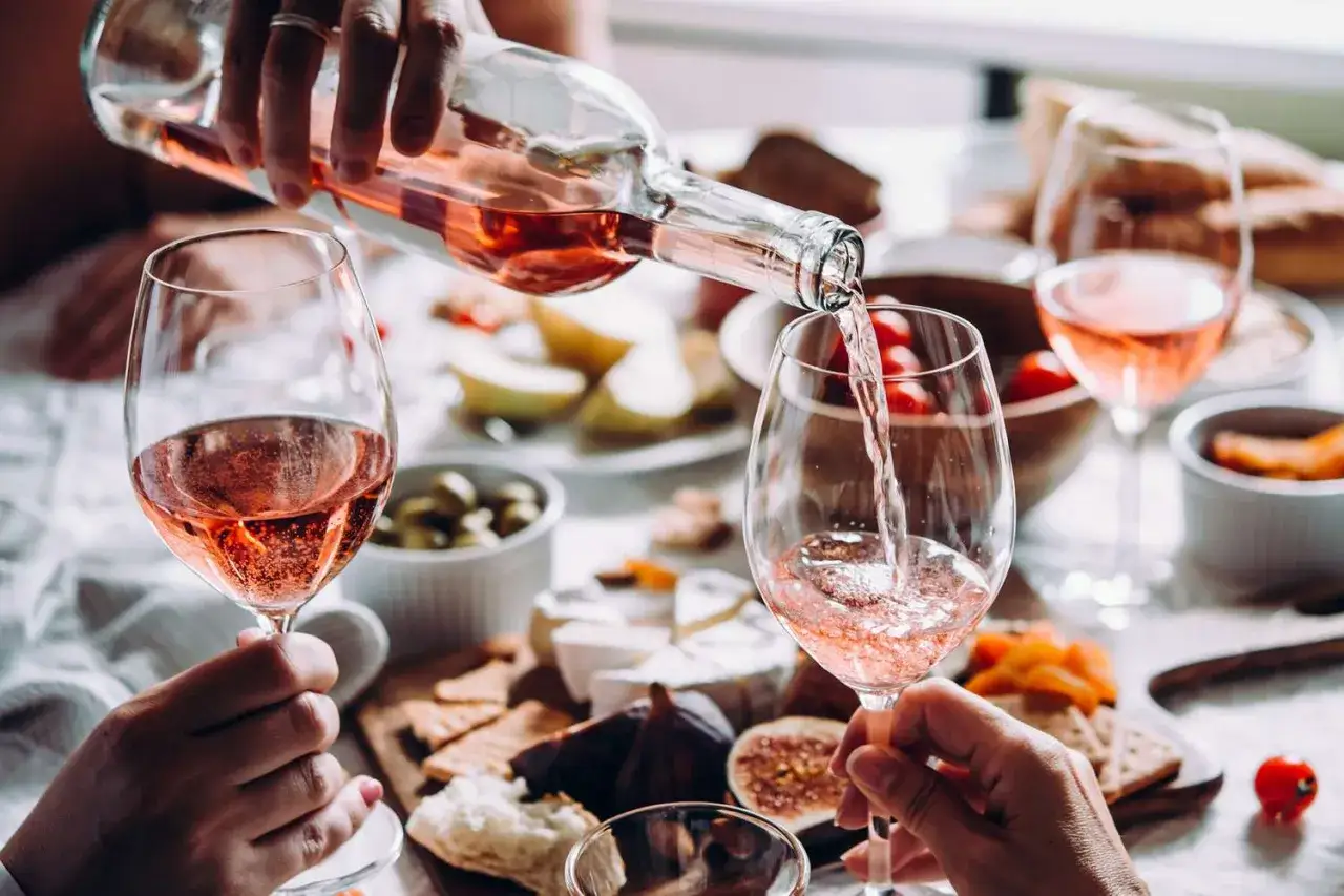 Pouring rosé wine, a delightful choice for a healthy indulgence, into a glass. A spread of cheese, crackers, and fruit suggests a perfect pairing.