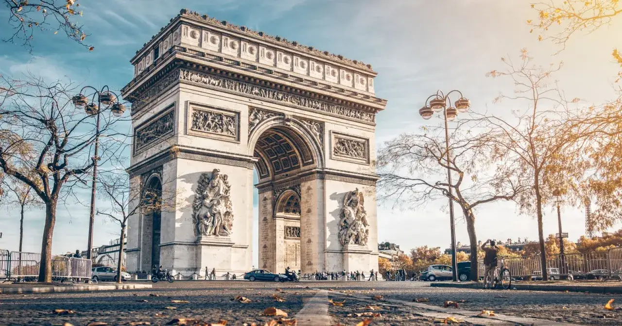 Arco del Triunfo en París, con el sol otoñal iluminando la avenida de los Campos Elíseos.