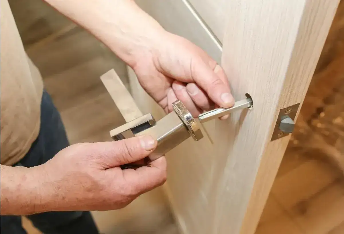 Hands assembling a modern door handle. A metal spindle is being inserted into the door mechanism, demonstrating how to replace door handle.