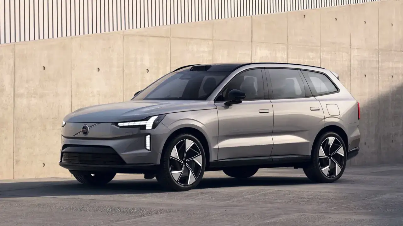Silver elbil 7 sits med modern design, parkerad framför en betongvägg med vertikala linjer.