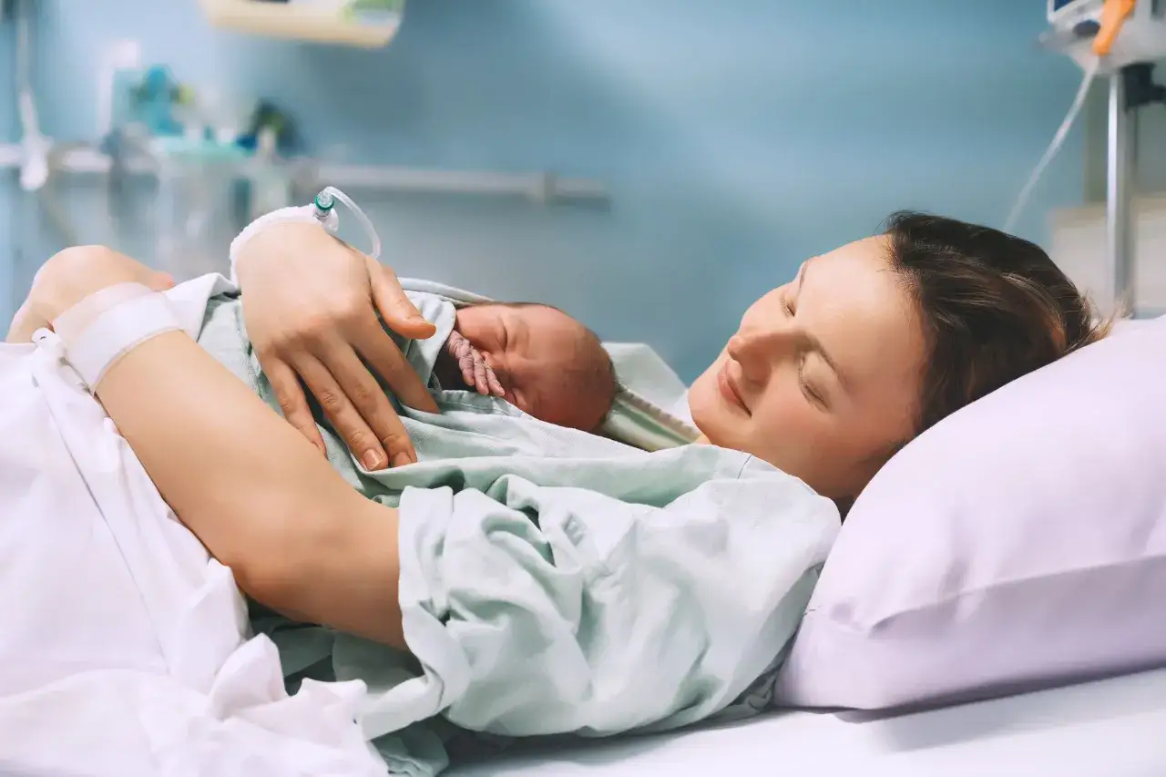 Szczęśliwa mama tuli noworodka po porodzie znieczulenie zewnątrzoponowe. Widoczny wenflon i opaska na ręce.