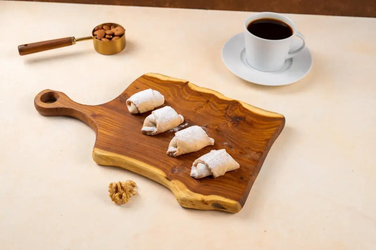 Vier mit Puderzucker best&auml;ubte Kurabiye-Kekse auf einem Holzbrett, daneben eine Tasse Kaffee und Mandeln. Ein perfektes kurabiye rezept f&uuml;r den Nachmittag.