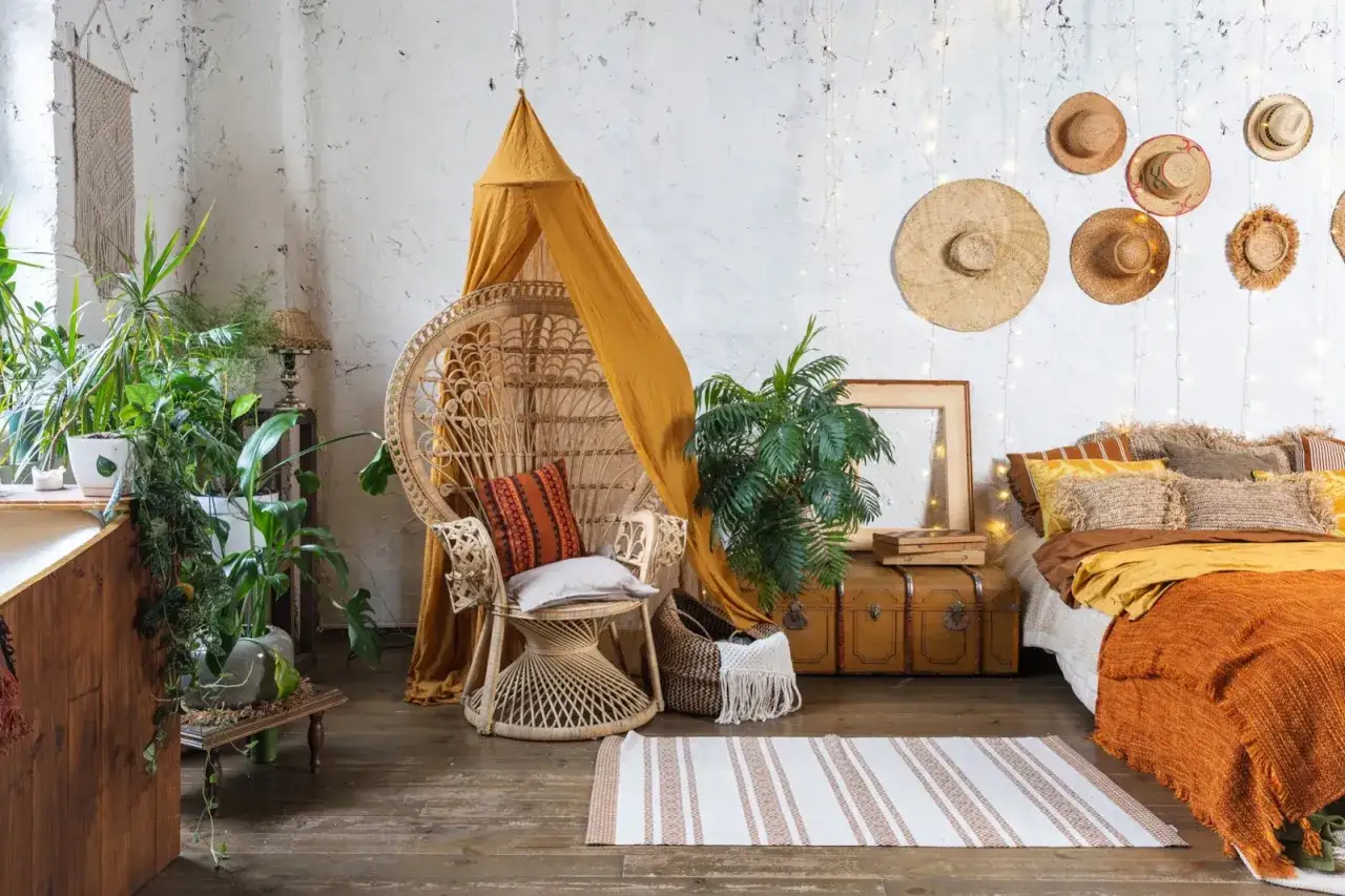 Sypialnia w stylu boho z wiklinowym fotelem, mnóstwem roślin i ozdobami z kapeluszy na ścianie.