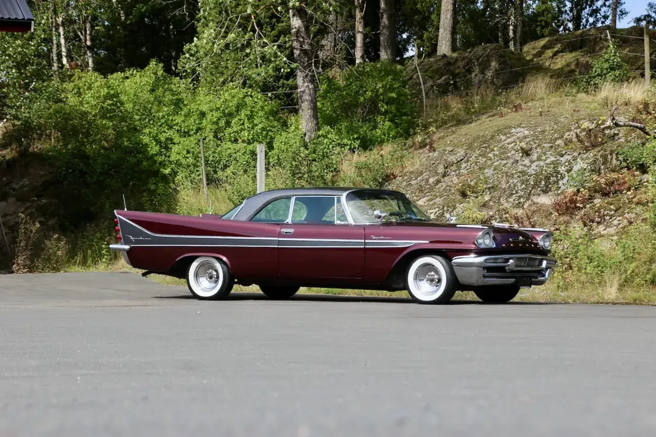 En vinr&ouml;d de soto bil med kromdetaljer och vita d&auml;cksidor st&aring;r parkerad p&aring; en asfalterad yta.
